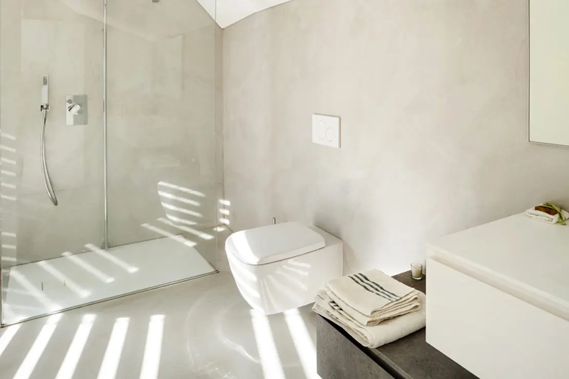 Baño con suelo y muros de microcemento en tonalidad luminosa.